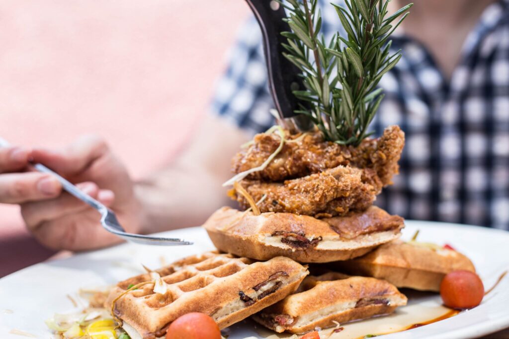 Sage Fried Chicken & Waffles from Hash House A Go Go at The LINQ, stacked high with rosemary garnish and served with maple syrup drizzle.