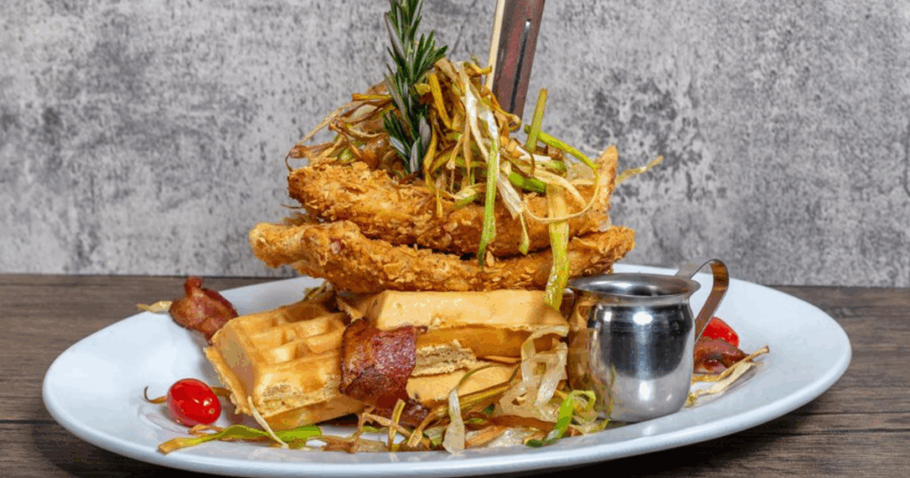 Menu favorite Sage Fried Chicken & Waffles from Hash House A Go Go at The LINQ in Las Vegas, served with bacon, leeks, and maple reduction.