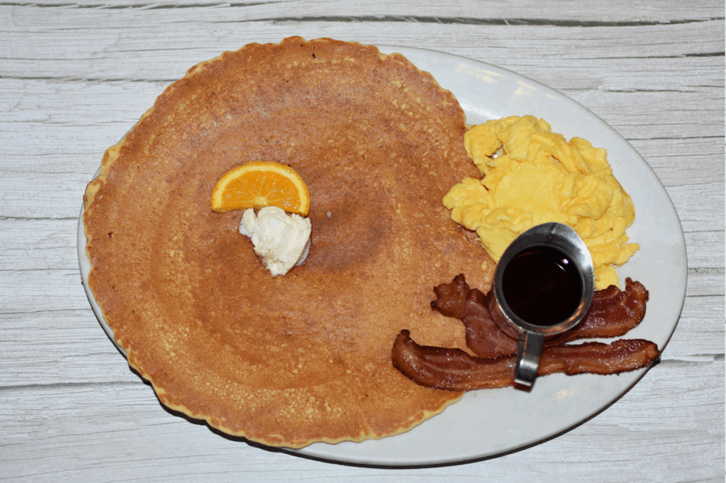 Comfort food at its finest with a giant pancake served with scrambled eggs, crispy bacon, syrup, and an orange slice at Hash House A Go Go at The LINQ